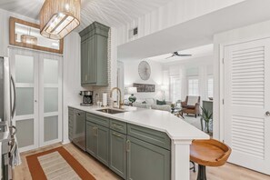 A kitchen with a large island, a dining area with a sofa, and a view of the living room. - Coastal Sage by Redfern (St. Simons Island)