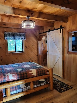 Ein Holzblock-Interieur mit einem Bett, einem Fenster, einer Tür und einer Deckenleuchte.