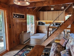 Ein Blockhauskaminareal mit Holzwänden, einer Treppe, einer Küchenzeile und einer Sitzecke mit einem gemusterten Teppich.