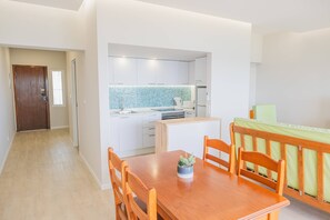 A modern kitchen with white cabinets, a blue backsplash, and a dining area with a wooden table and chairs. - Apartament Sea View 6F (Portimão)