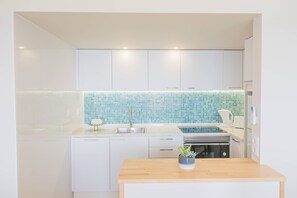 A modern kitchen with white cabinets, a blue-tiled backsplash, and a wooden countertop. - Apartament Sea View 6F (Portimão)