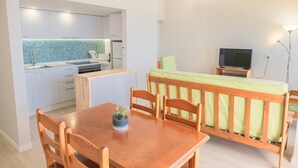 Ett kompakt bostadsutrymme med ett litet kök, en matplats och en sovplats med TV.