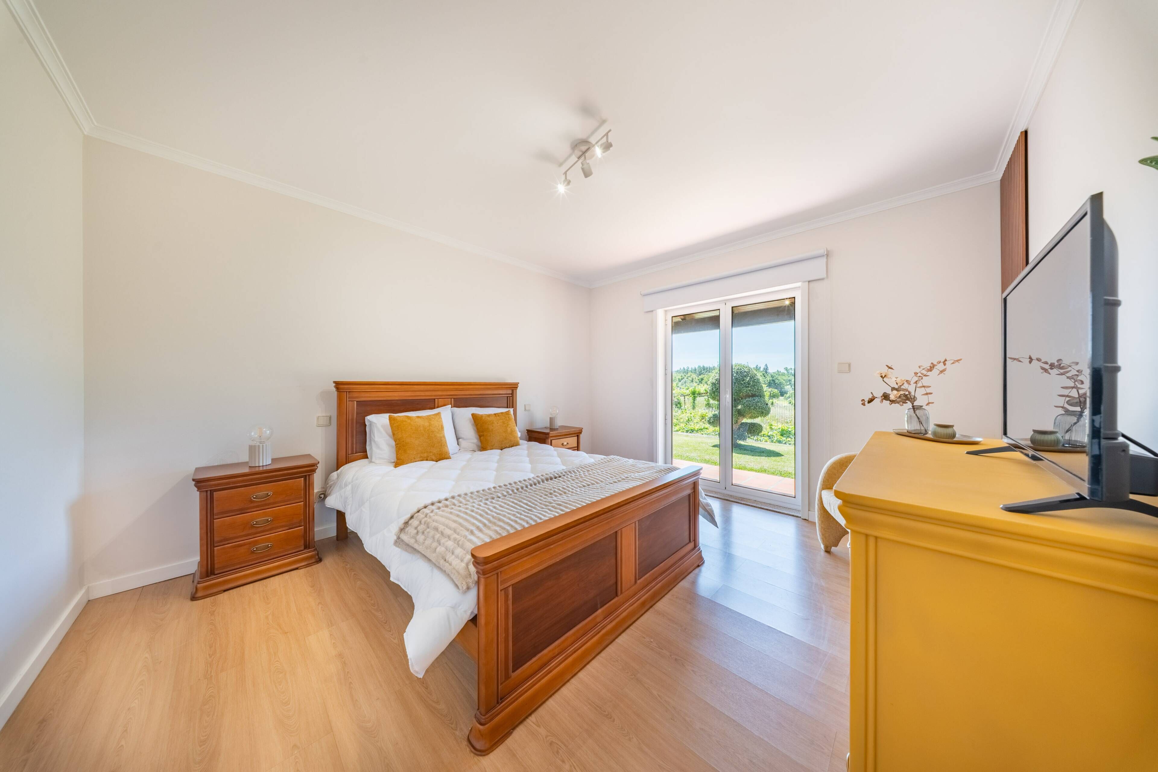 Un dormitorio con una cama de madera, una mesita de noche, un aparador y un televisor.