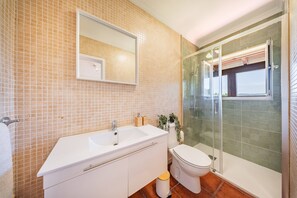 Une salle de bain avec un lavabo blanc, un miroir et des toilettes, une douche en verre et un mur carrelé.