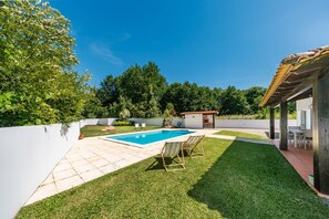 Un jardin avec une piscine, un espace patio et un petit bâtiment.