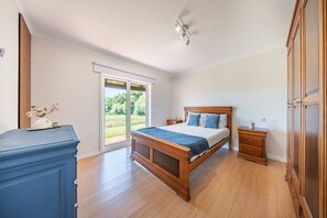 Une chambre à coucher avec un lit en bois, une table de chevet, une commode et une porte-fenêtre coulissante donnant sur un balcon.