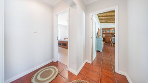 Un corridoio con pareti bianche e pavimento piastrellato che conduce a una sala da pranzo con mobili e sedie in legno.