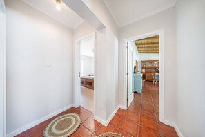 Ein Flur mit weißen Wänden und gefliestem Boden, der zu einem Essbereich mit Holzausstattung und Stühlen führt.