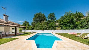 Una piscina rettangolare con bordo piastrellato, circondata da un prato e alberi.