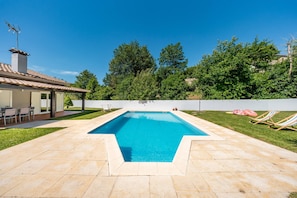 Ein rechteckiger Pool mit Fliesen umgeben von einer Rasenfläche und Bäumen.