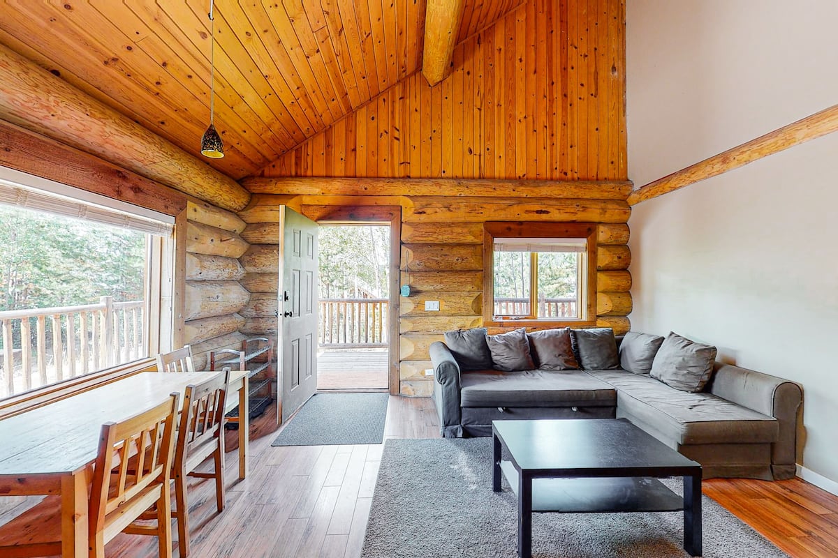 A log cabin interior with a dining area, sofa, and a view through the door.