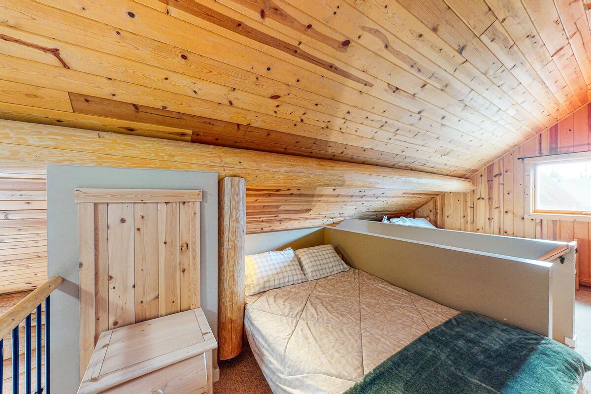 A wooden cabin bedroom with a bunk bed and a single bed, wooden walls, and a window.