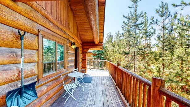 Una cabaña de madera con terraza, mobiliario exterior y vistas a árboles.