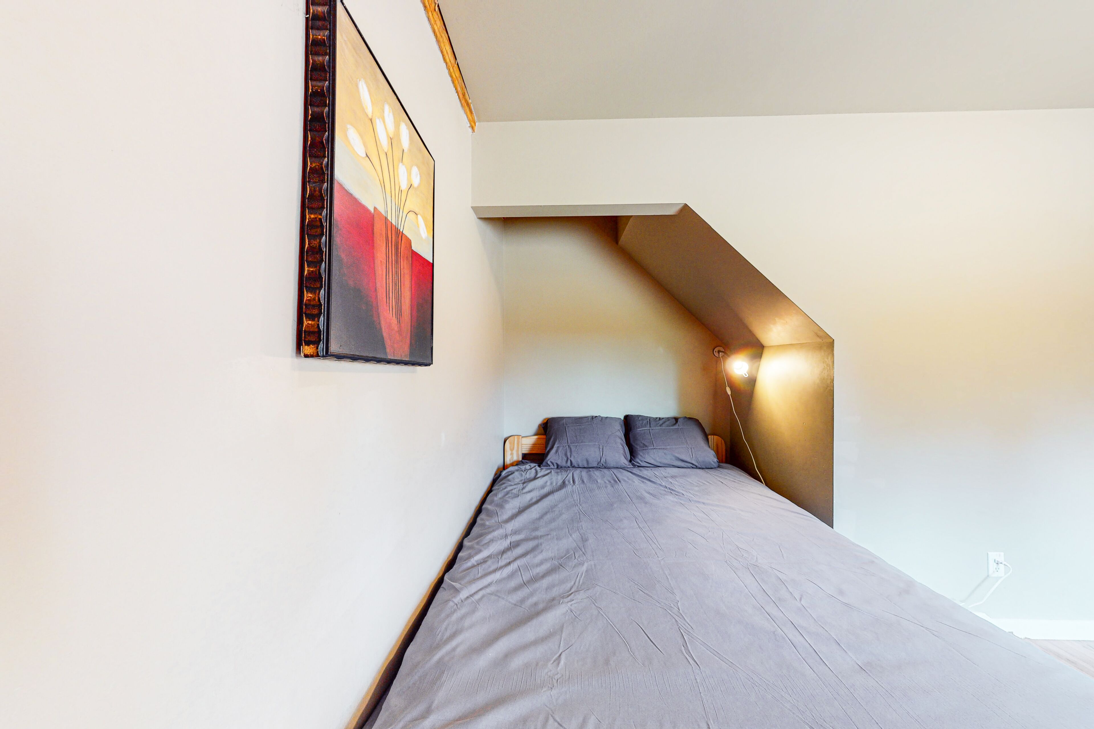 A bedroom with a bed, a painting on the wall, and a sloped ceiling.
