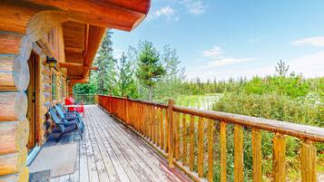 A wooden deck with a railing, a covered seating area, and a view of a pond and trees.