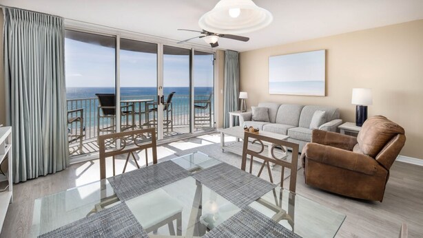 A spacious living room with a glass table, a sofa, a brown armchair, and a balcony with a view of the ocean. - Island Princess 608🌊Gulf Front🏖️Free Beach Setup (Fort Walton Beach)