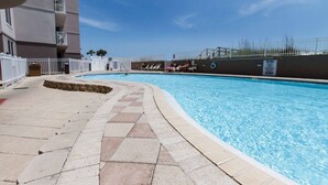 A swimming pool with a tiled deck, a white fence, and a building with balconies in the background. - Island Princess 608🌊Gulf Front🏖️Free Beach Setup (Fort Walton Beach)