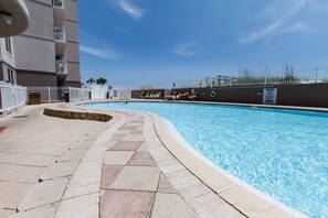 A swimming pool with a tiled deck, a white fence, and a building with balconies in the background. - Island Princess 608🌊Gulf Front🏖️Beach Service (Fort Walton Beach)