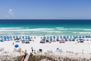 A beach with rows of blue umbrellas and beach chairs, a wooden boardwalk, and a clear view of the ocean. - Island Princess 608🌊Gulf Front🏖️Beach Service (Fort Walton Beach)