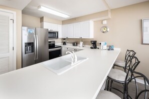 A modern kitchen with white cabinets, stainless steel appliances, a built-in microwave, and a sink. - Island Princess 608🌊Gulf Front🏖️Beach Service (Fort Walton Beach)
