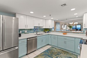 Une cuisine moderne dotée d’appareils électroménagers en acier inoxydable, de meubles de couleur bleu clair et d’un revêtement mural composé de carreaux bleus et verts.