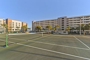 Ein Tennisplatz mit Netz, umzäunt und neben einem mehrstöckigen Gebäude mit Balkonen.