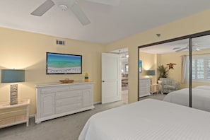A bedroom with a bed, a dresser, a television, and a door leading to another room. - Surf Dweller 207🌊Gulf Front🏖️2 Free Beach Setups (Fort Walton Beach)
