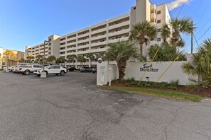 Un parking avec plusieurs voitures, un bâtiment sur lequel on peut lire l’inscription « Surf Dwellers », et des palmiers.