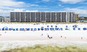 A beachfront hotel with multiple floors, beach umbrellas, and a sandy beach. - Surf Dweller 207🌊Gulf Front🏖️Beach Service (Fort Walton Beach)