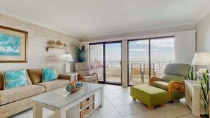 Ein geräumiger Wohnbereich mit Sofa, Hocker und Couchtisch, ein Balkon mit Aussicht und ein großes Fenster.