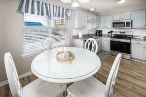 A kitchen with white cabinets, a microwave, stove, and a dining table with chairs. - Sunset Cottages 5C 🏖️Free Beach Setup (Fort Walton Beach)