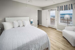 Ein Schlafzimmer mit einem großen Bett, einem Nachttisch, einer Lampe, einem Fenster mit Jalousien und einer Tür zu einem weiteren Raum.