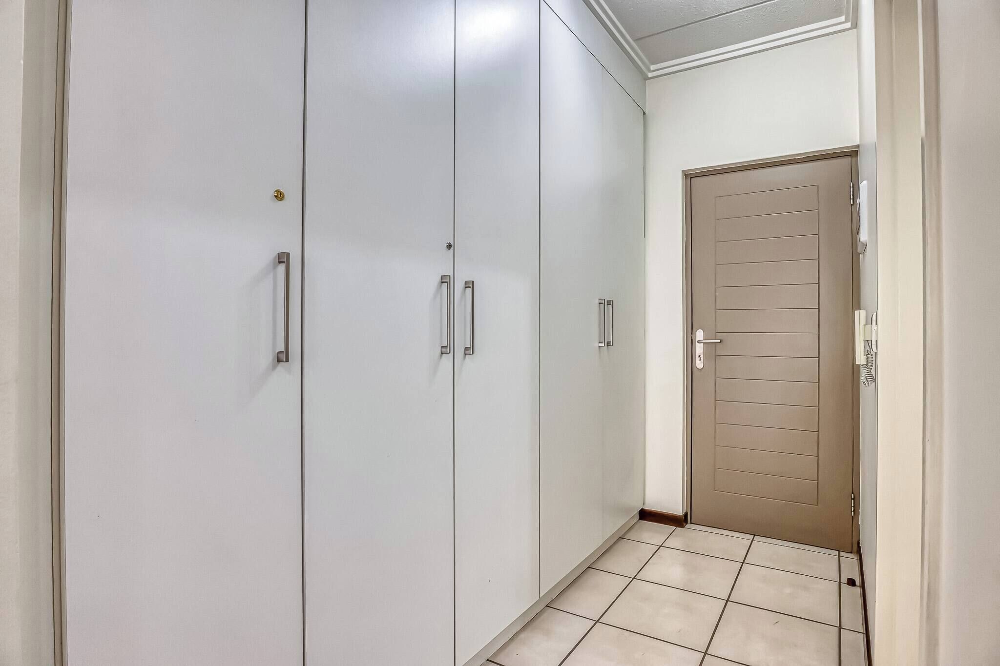 Um corredor com um armário branco grande, uma porta bege e piso ladrilhado.