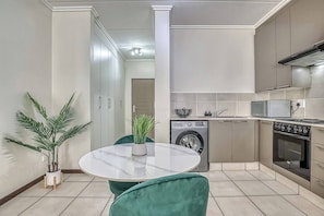 A modern kitchen with a round table, green chairs, a washing machine, and a stove. - Cozy Studio Apartment in Paulshof, Sandton - Perfect for Extended Stays (Johannesburg)