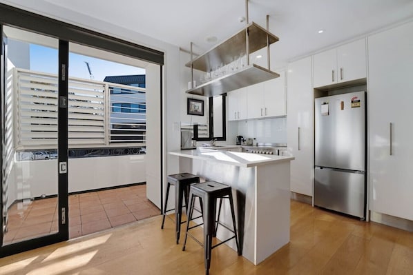 Una cocina moderna con una isla central, electrodomésticos de acero inoxidable y vista a un edificio.