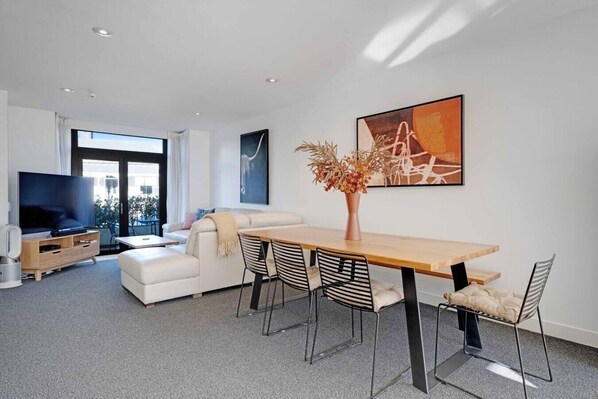 A modern living room with a sofa, TV, dining table, and chairs.