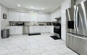 Una cocina moderna con armarios blancos, electrodomésticos de acero inoxidable y piso de mármol.