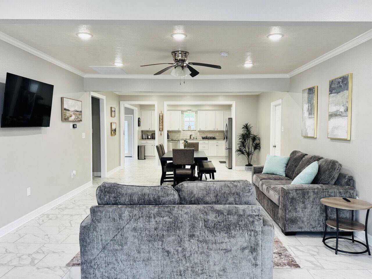 A spacious living room with a gray sofa, a gray armchair, and a dining area with a table and chairs.