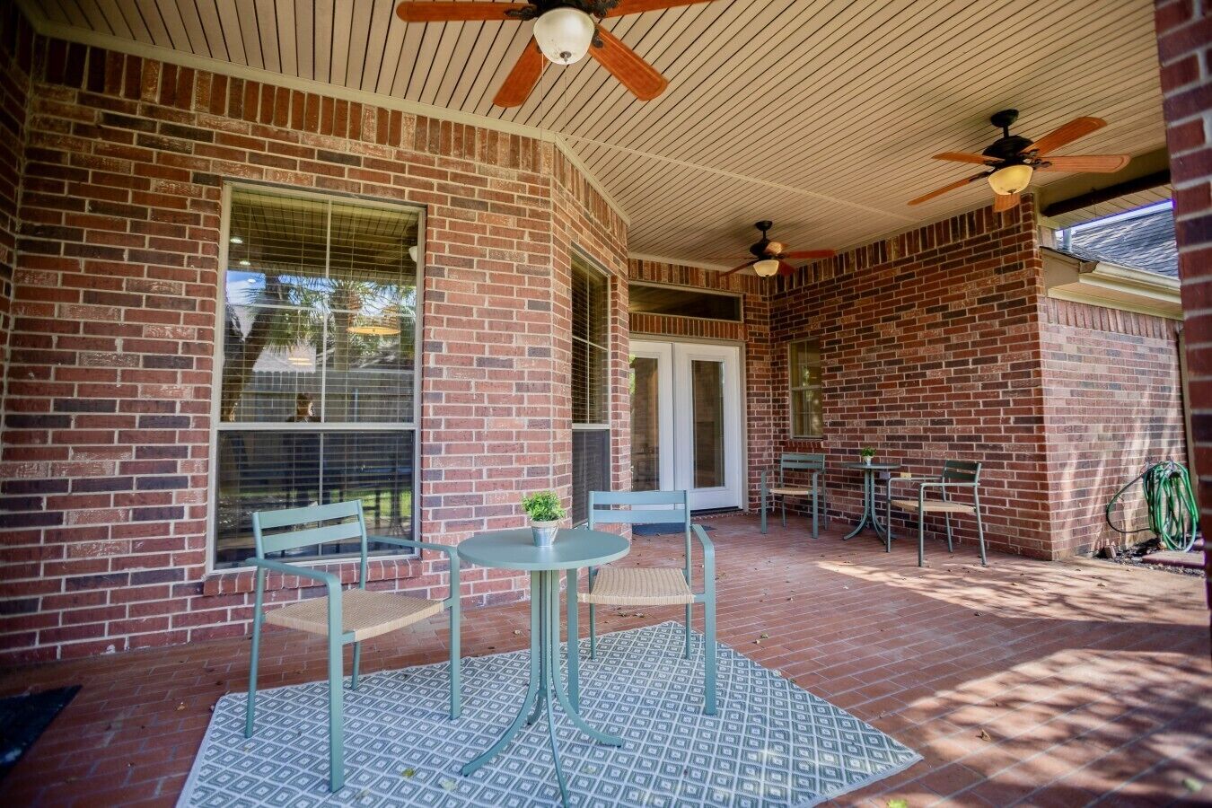 A covered patio with brick walls, a ceiling fan, and a table with chairs.