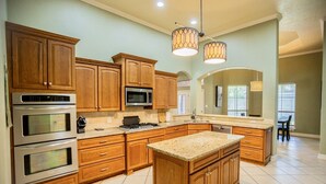 A kitchen with wooden cabinets, stainless steel appliances, a granite countertop, and pendant lighting. - Where style meets comfort (Orange)
