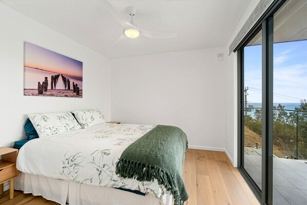 A bedroom with a bed, a nightstand, a large window, and a ceiling fan.