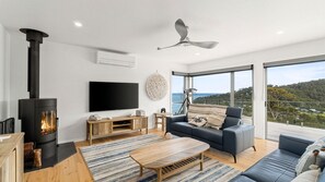 Ein modernes Wohnzimmer mit Kamin, Flachbildfernseher, Sofa, Couchtisch und einem Balkon mit Blick.