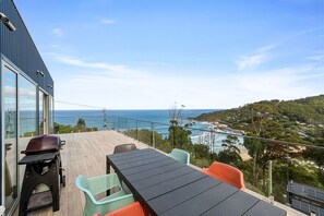 A balcony with a view of the sea, outdoor furniture, and a grill.
