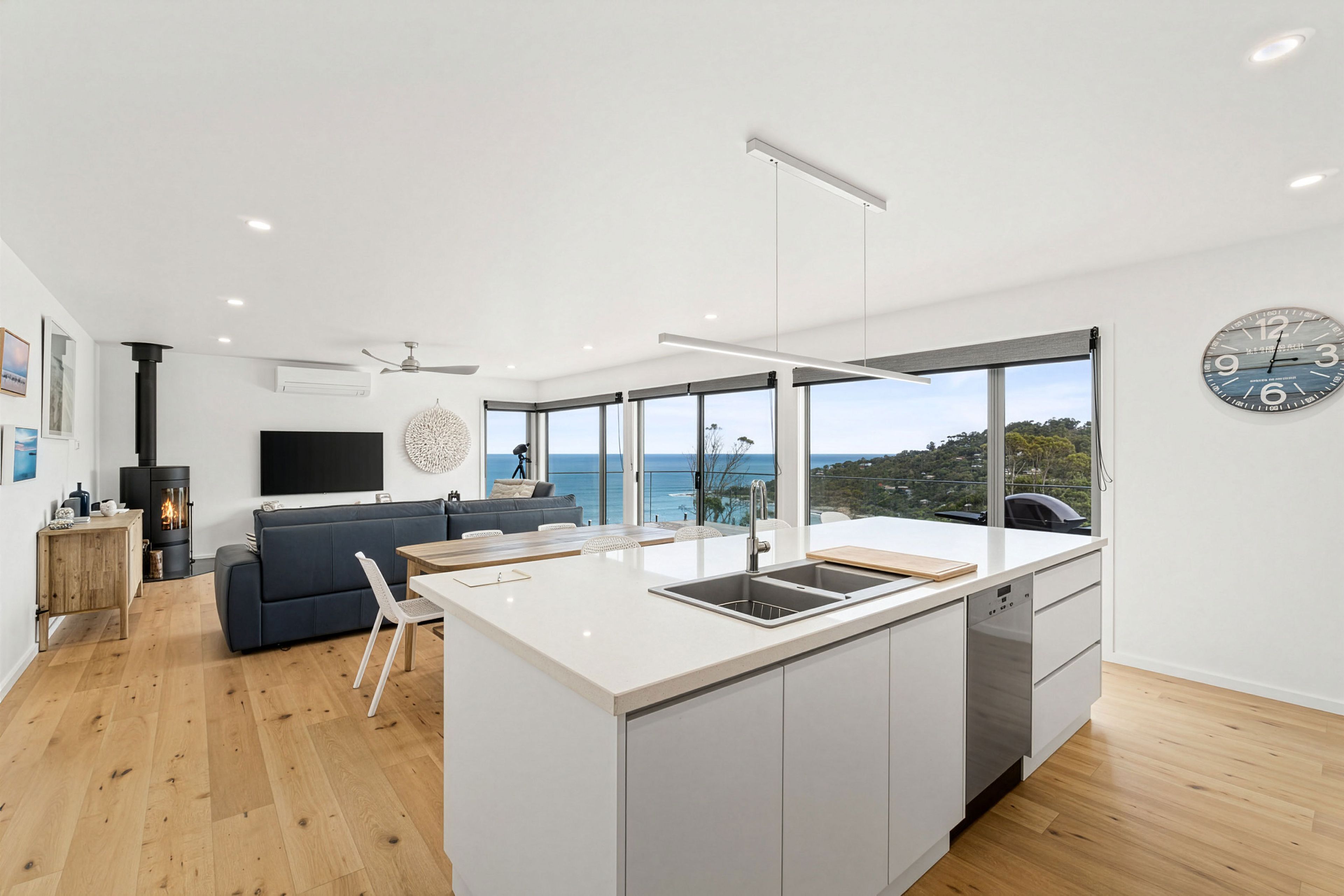 A modern kitchen with a central island, large windows, and a view of the sea.
