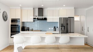 Une cuisine moderne dotée d’un îlot central, de tabourets de bar et d’un réfrigérateur en acier inoxydable.