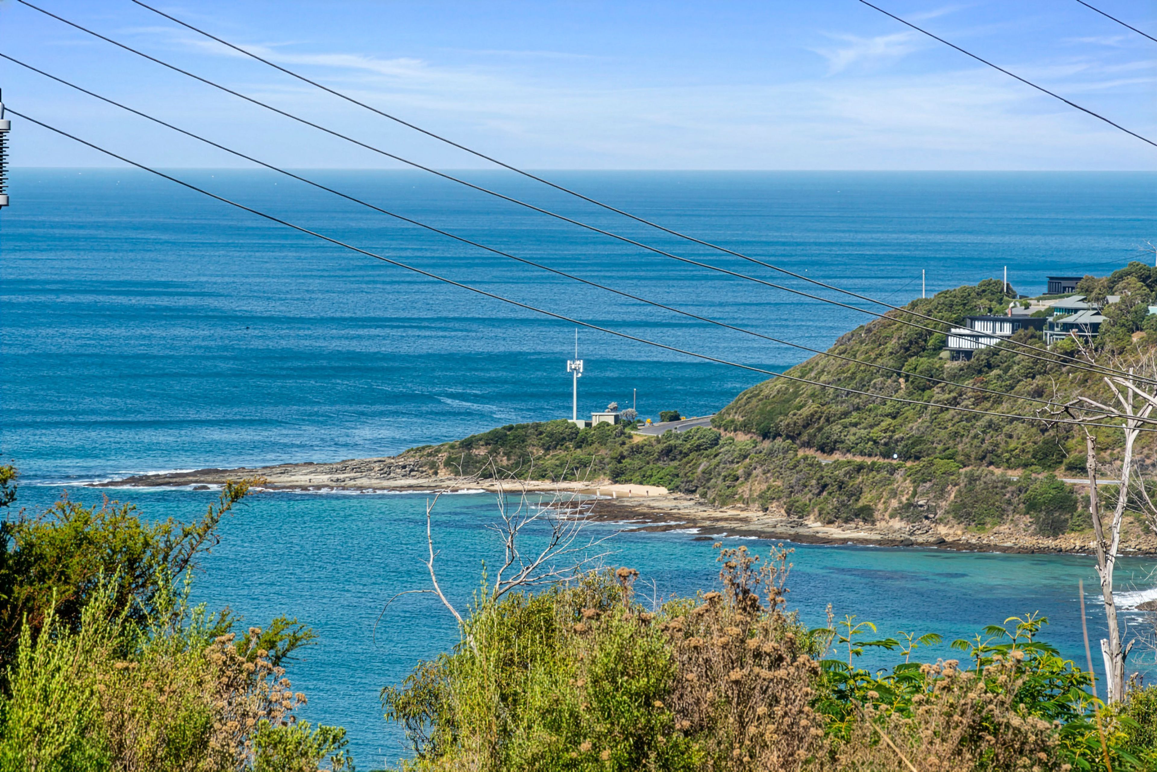 A coastal landscape with a clear view of the sea, a hill with buildings, and power lines overhead.