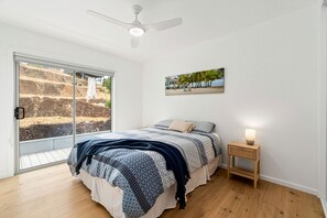Ein Schlafzimmer mit einem Bett, einem Nachttisch, einem Deckenventilator, einem Fenster mit Landschaftsblick und einem Bild an der Wand.