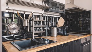 Cocina moderna con salpicadero de azulejos negros, electrodomésticos de acero inoxidable, encimera de madera y utensilios colgantes.