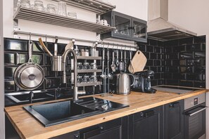 A modern kitchen with black tiled backsplash, stainless steel appliances, wooden countertop, and hanging utensils. - Diente | Studio | Poznań Jeżyce | Balkon & Kamienica (Poznań)