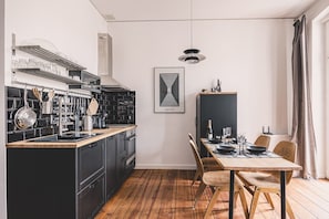 A modern kitchen with black cabinetry, a wooden dining table, and a hanging pendant light. - Diente | Studio | Poznań Jeżyce | Balkon & Kamienica (Poznań)